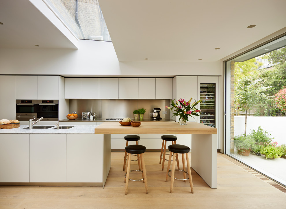 Bild på ett minimalistiskt kök, med släta luckor, vita skåp, ljust trägolv, en köksö och integrerade vitvaror
