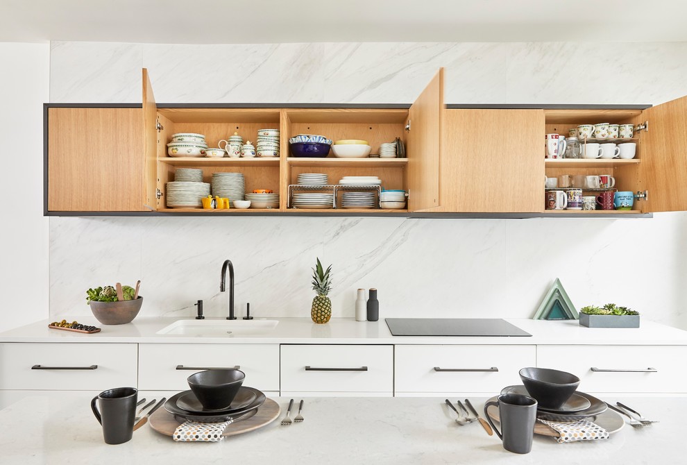 Modern inredning av ett mellanstort vit vitt kök, med en undermonterad diskho, släta luckor, skåp i ljust trä, bänkskiva i kvarts, vitt stänkskydd, stänkskydd i marmor, integrerade vitvaror, klinkergolv i porslin, en köksö och svart golv