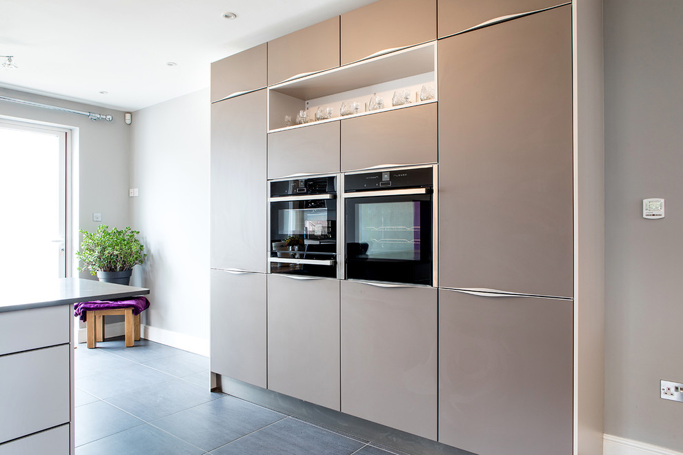 Photo of a medium sized contemporary u-shaped kitchen/diner in Surrey with a submerged sink, flat-panel cabinets, grey cabinets, quartz worktops, glass sheet splashback, integrated appliances, a breakfast bar and grey worktops.