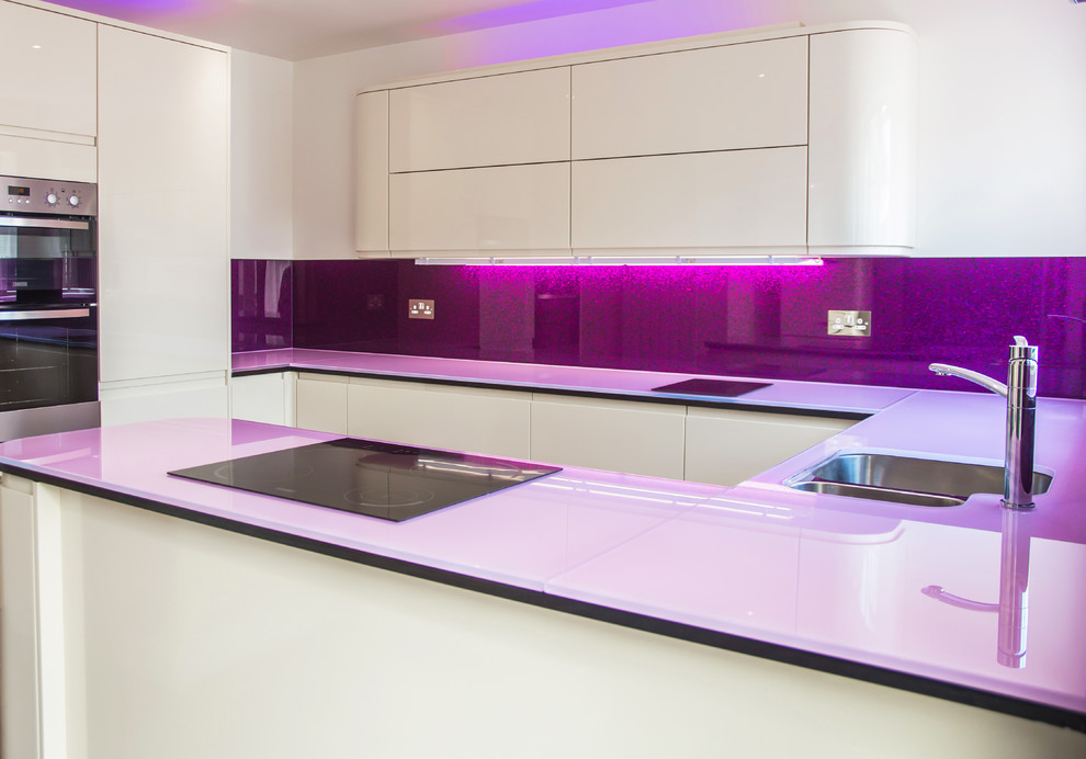 Inspiration for a large contemporary u-shaped enclosed kitchen in London with glass worktops, glass sheet splashback, a submerged sink, flat-panel cabinets, white cabinets, metallic splashback, stainless steel appliances and an island.