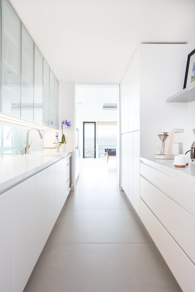 Modelo de cocina contemporánea sin isla con armarios con paneles lisos, puertas de armario blancas, salpicadero de vidrio templado y suelo gris