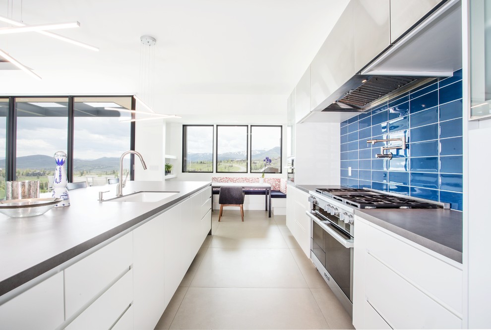 На фото: параллельная кухня в современном стиле с врезной мойкой, плоскими фасадами, белыми фасадами, синим фартуком, островом и серым полом