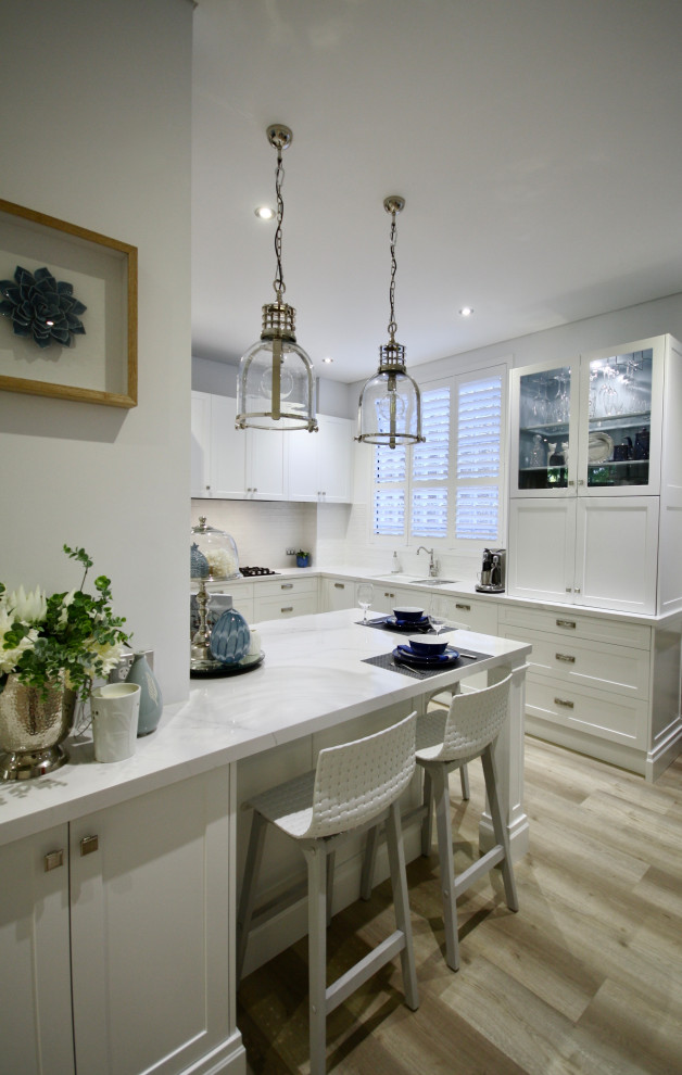 Exempel på ett mellanstort klassiskt vit vitt kök, med en undermonterad diskho, skåp i shakerstil, vita skåp, bänkskiva i kvarts, vitt stänkskydd, stänkskydd i tunnelbanekakel, rostfria vitvaror, ljust trägolv, en köksö och brunt golv