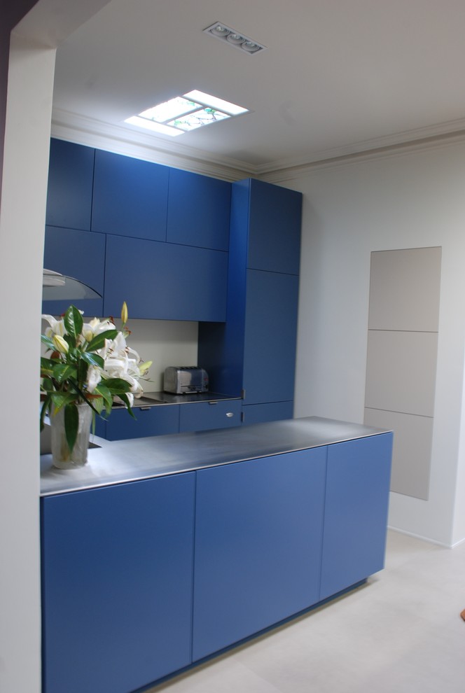 Inredning av ett modernt litet kök, med släta luckor, en integrerad diskho, blå skåp, bänkskiva i rostfritt stål, grått stänkskydd, glaspanel som stänkskydd, betonggolv, en halv köksö och grått golv