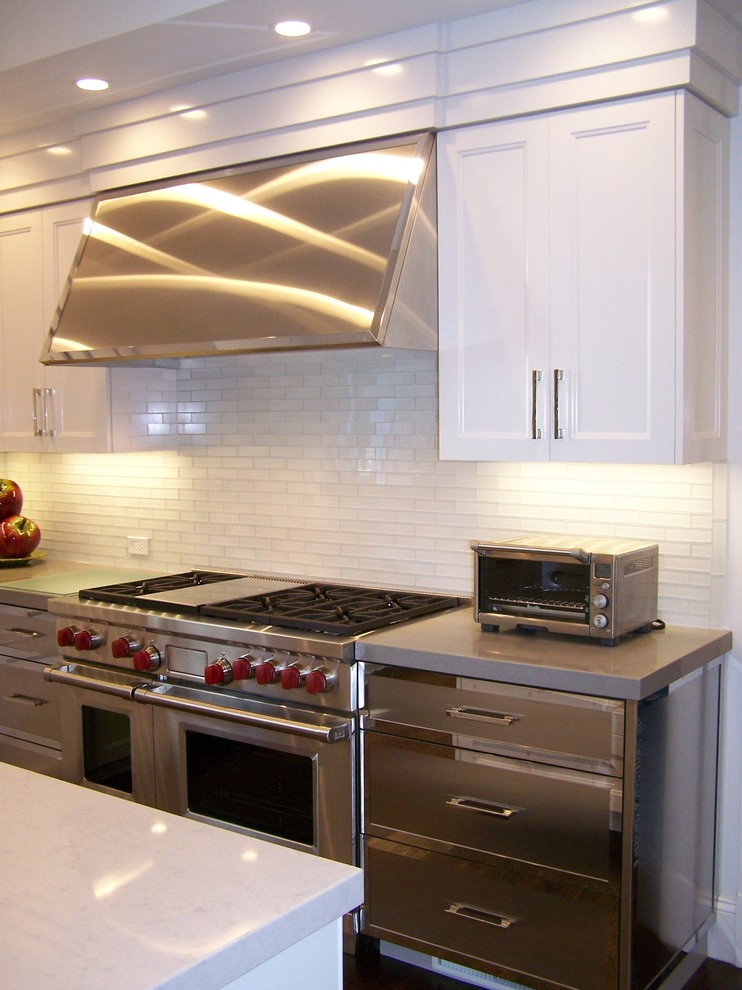 Inredning av ett kök, med en köksö, luckor med infälld panel, vitt stänkskydd, stänkskydd i tunnelbanekakel, rostfria vitvaror och mörkt trägolv