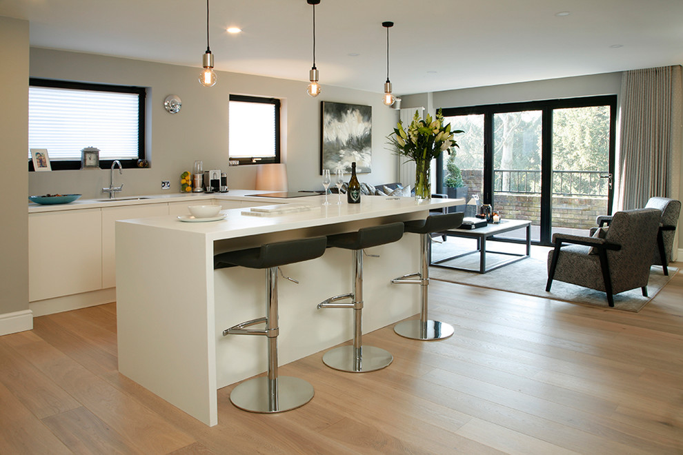 Medium sized classic u-shaped open plan kitchen in London with a built-in sink, flat-panel cabinets, white cabinets, composite countertops, white appliances, light hardwood flooring and a breakfast bar.