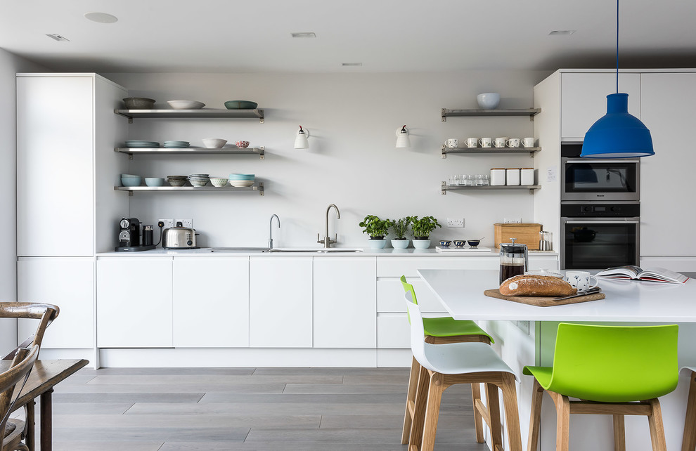 Eat-in kitchen - contemporary light wood floor eat-in kitchen idea in London with an undermount sink, flat-panel cabinets, white cabinets, solid surface countertops, white backsplash, stainless steel appliances and an island