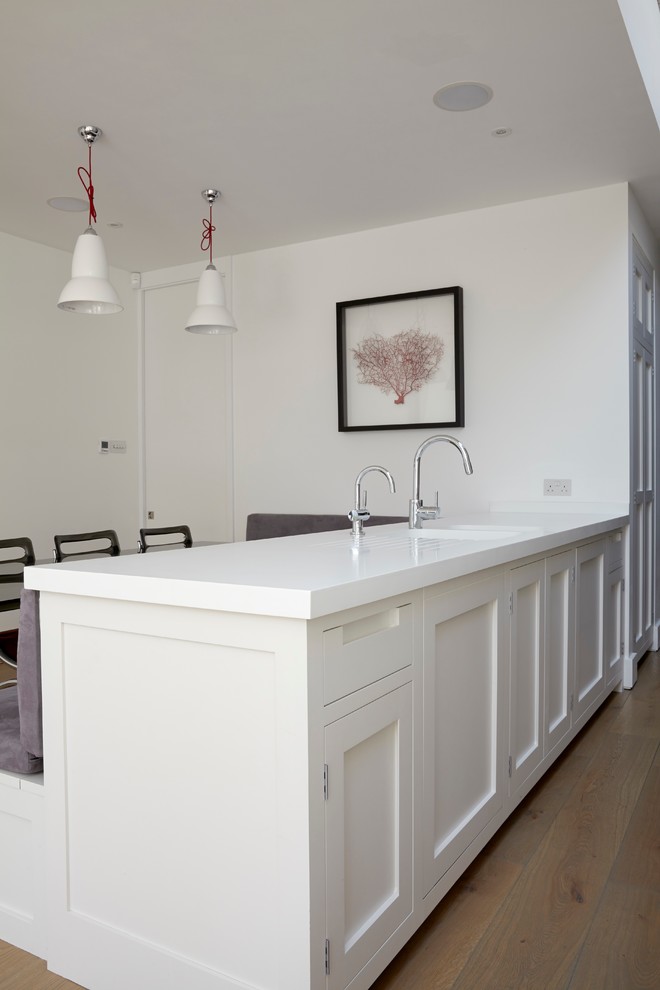 Bild på ett mellanstort funkis kök, med en dubbel diskho, skåp i shakerstil, vita skåp, bänkskiva i koppar, vitt stänkskydd, glaspanel som stänkskydd, integrerade vitvaror, ljust trägolv och en köksö