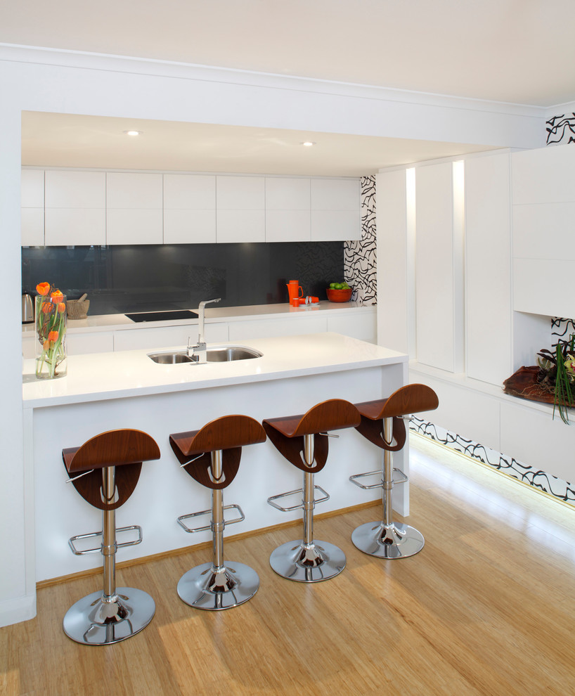 Photo of a contemporary kitchen in Sydney with flat-panel cabinets, black splashback, a breakfast bar and light hardwood flooring.