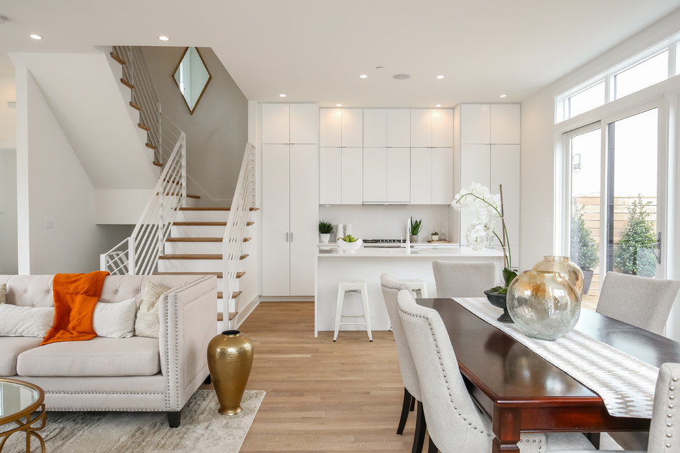 Modern inredning av ett vit vitt kök med öppen planlösning, med släta luckor, vita skåp, en köksö, vitt stänkskydd, ljust trägolv och brunt golv