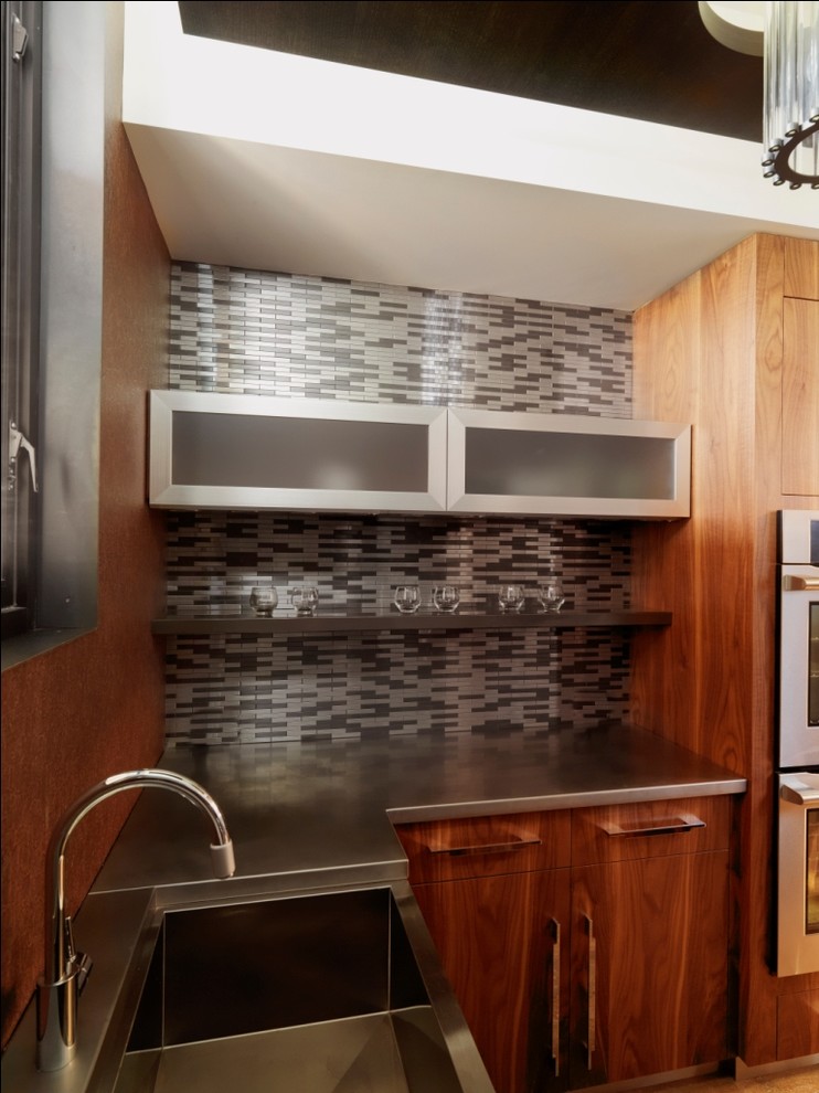 Aménagement d'une cuisine montagne en bois brun avec un évier intégré, un placard à porte plane, un plan de travail en inox et une crédence multicolore.