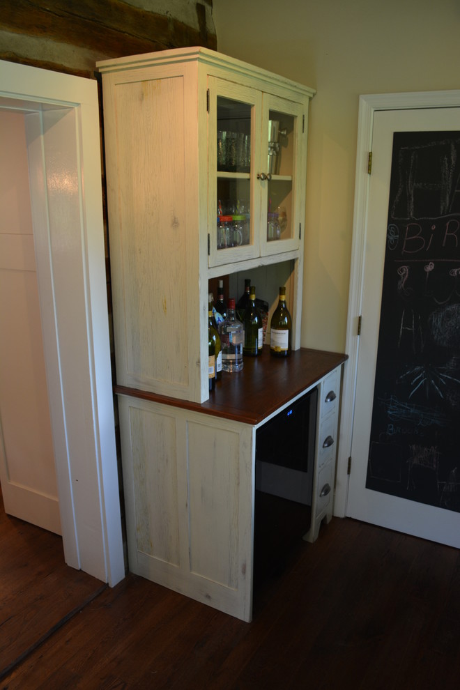 Foto på ett litet lantligt kök, med en rustik diskho, luckor med infälld panel, vita skåp, bänkskiva i täljsten, beige stänkskydd, stänkskydd i stenkakel, rostfria vitvaror, mellanmörkt trägolv och en köksö