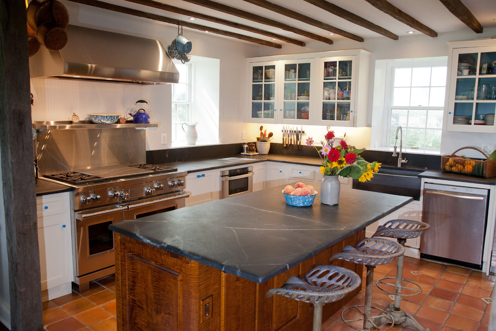 Modelo de cocina campestre, grande, con fregadero sobremueble, armarios estilo shaker, puertas de armario blancas, encimera de esteatita, electrodomésticos de acero inoxidable y suelo de baldosas de cerámica