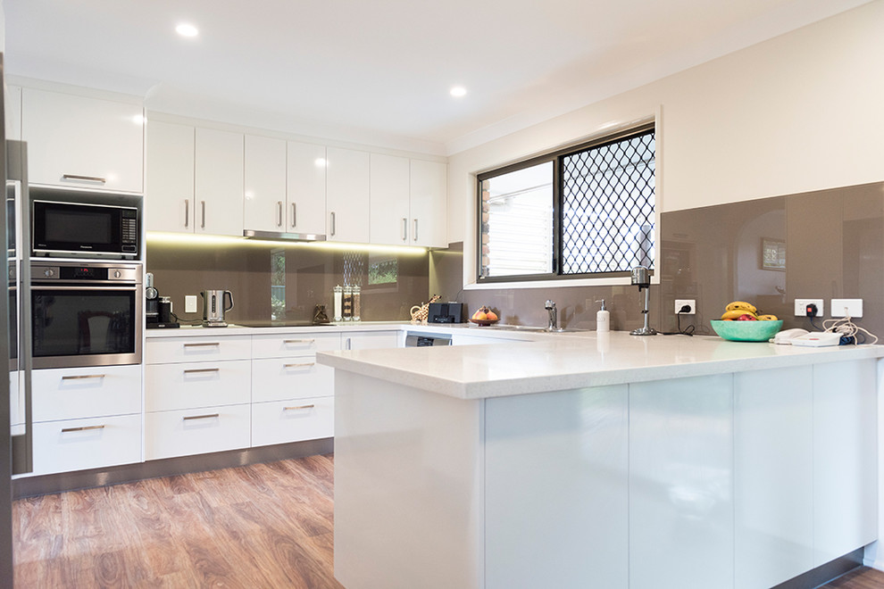 Einzeilige, Mittelgroße Moderne Wohnküche mit Einbauwaschbecken, flächenbündigen Schrankfronten, weißen Schränken, Marmor-Arbeitsplatte, Küchenrückwand in Weiß, Rückwand aus Keramikfliesen, weißen Elektrogeräten, dunklem Holzboden, Kücheninsel und braunem Boden in Brisbane