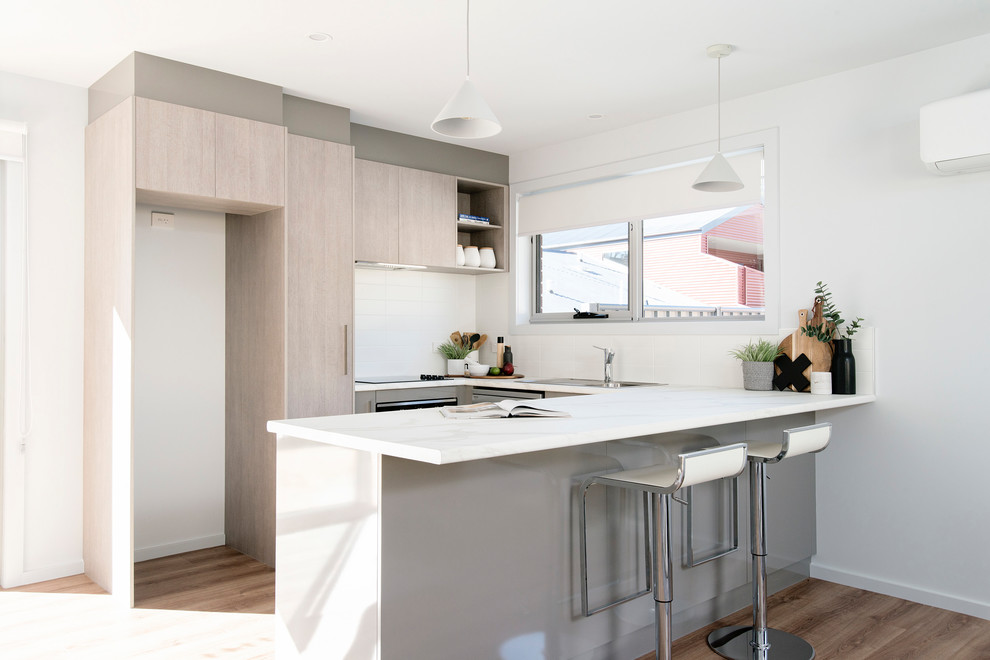 Inredning av ett modernt litet grå grått kök, med en nedsänkt diskho, luckor med infälld panel, skåp i ljust trä, laminatbänkskiva, vitt stänkskydd, stänkskydd i keramik, rostfria vitvaror, vinylgolv och brunt golv