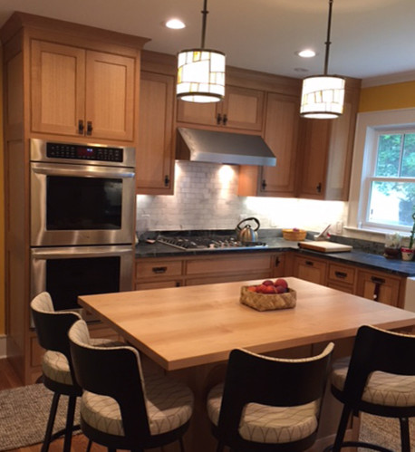 Mid-sized arts and crafts l-shaped medium tone wood floor enclosed kitchen photo in New York with a farmhouse sink, shaker cabinets, medium tone wood cabinets, wood countertops, gray backsplash, stone tile backsplash, stainless steel appliances and an island