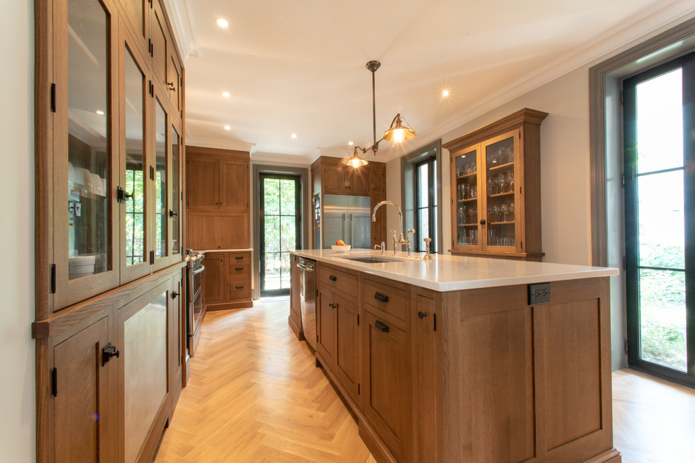 Imagen de cocina de estilo americano de tamaño medio con fregadero bajoencimera, armarios estilo shaker, puertas de armario de madera oscura, encimera de cuarzo compacto, salpicadero blanco, salpicadero de azulejos de cerámica, electrodomésticos de acero inoxidable, suelo de madera clara, una isla y encimeras blancas