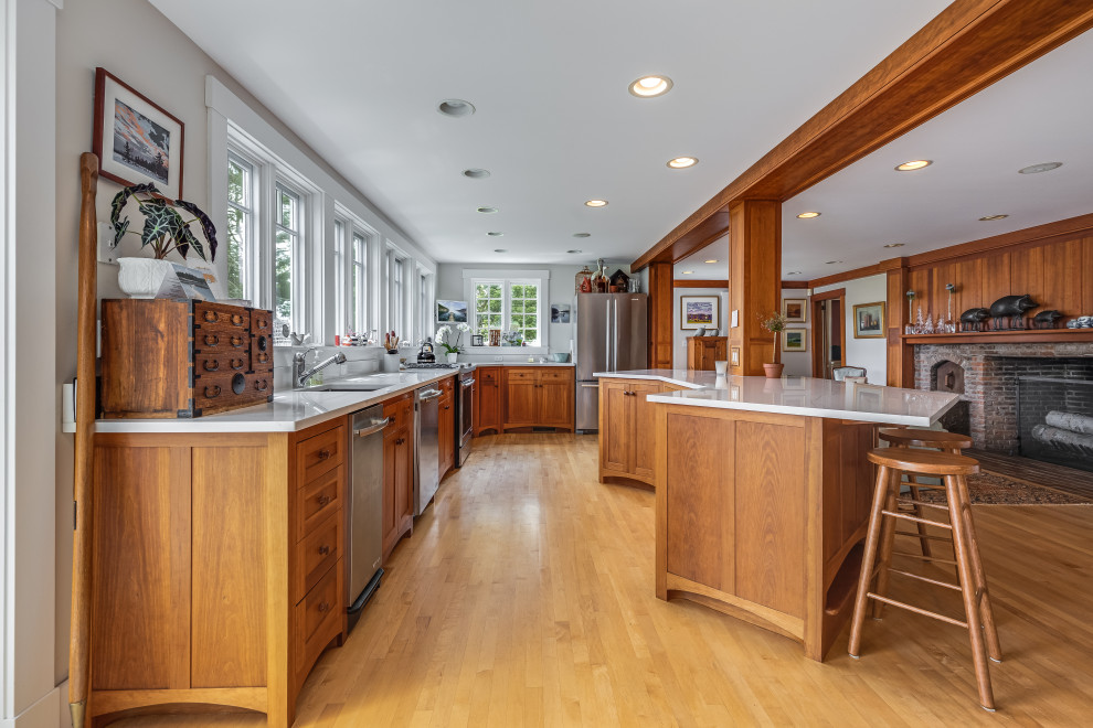 Photo of a large nautical u-shaped kitchen in Boston with a single-bowl sink, medium wood cabinets, engineered stone countertops, stainless steel appliances, light hardwood flooring, an island, white worktops, shaker cabinets and beige floors.