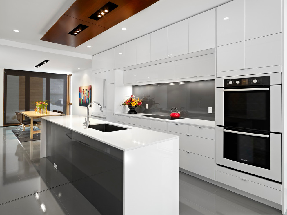 Inredning av ett modernt kök och matrum, med en integrerad diskho, släta luckor, grått stänkskydd, stänkskydd i glaskakel, integrerade vitvaror, en köksö, grått golv och vita skåp