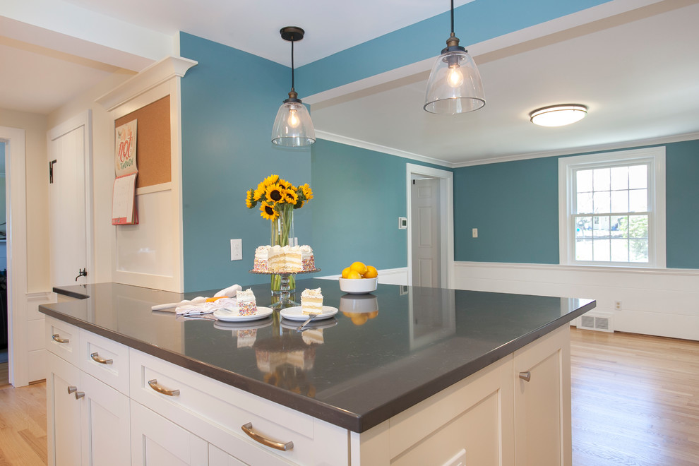 Example of a mid-sized trendy l-shaped light wood floor and yellow floor eat-in kitchen design in Bridgeport with a single-bowl sink, recessed-panel cabinets, white cabinets, quartzite countertops, beige backsplash, limestone backsplash, stainless steel appliances, a peninsula and black countertops
