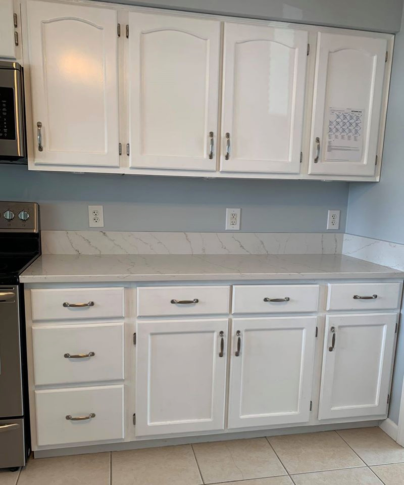 Foto på ett litet maritimt vit kök, med en undermonterad diskho, luckor med infälld panel, vita skåp, bänkskiva i kvarts, klinkergolv i keramik och brunt golv