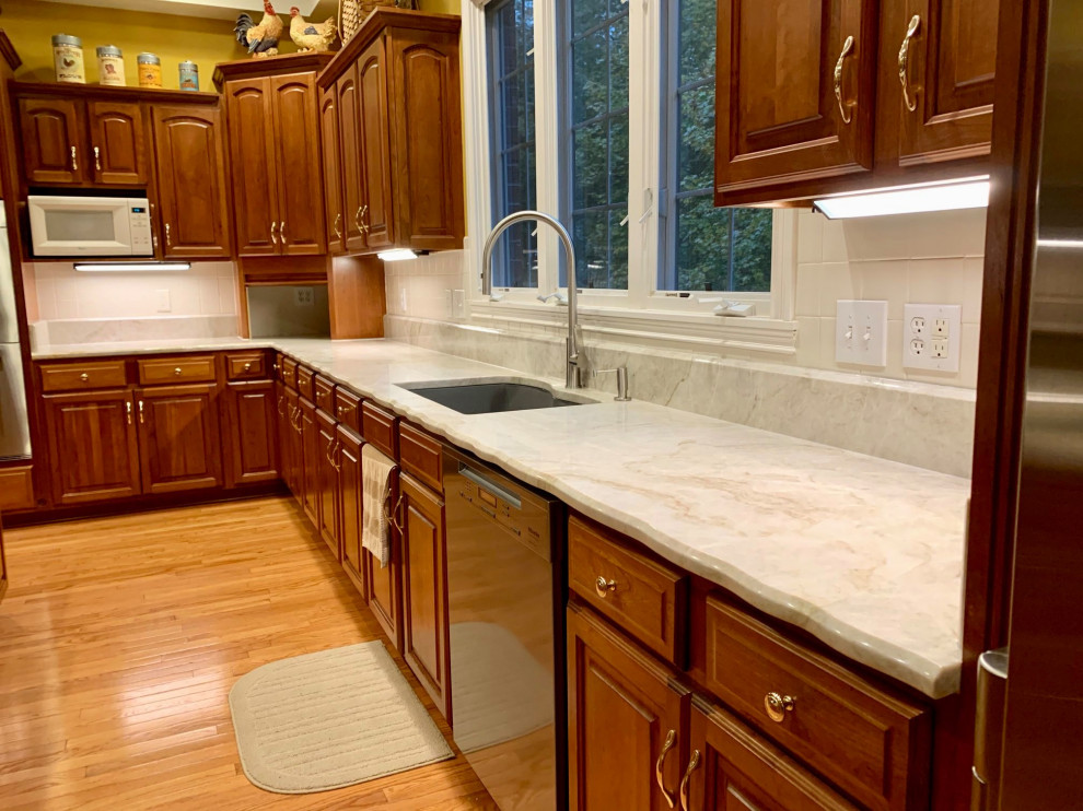 Photo of a large traditional l-shaped kitchen/diner in Indianapolis with a submerged sink, raised-panel cabinets, medium wood cabinets, quartz worktops, white splashback, ceramic splashback, stainless steel appliances, medium hardwood flooring, an island, brown floors and white worktops.