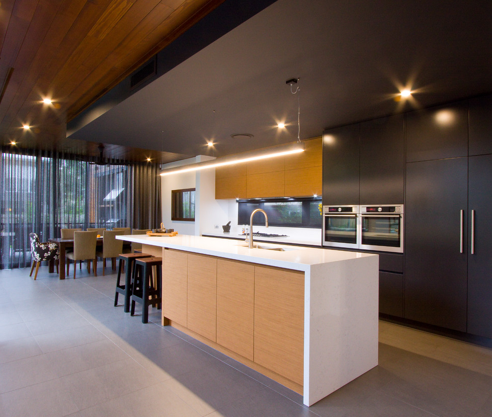 Стильный дизайн: параллельная кухня в современном стиле с обеденным столом, плоскими фасадами, черными фасадами, техникой из нержавеющей стали, островом и серым полом - последний тренд
