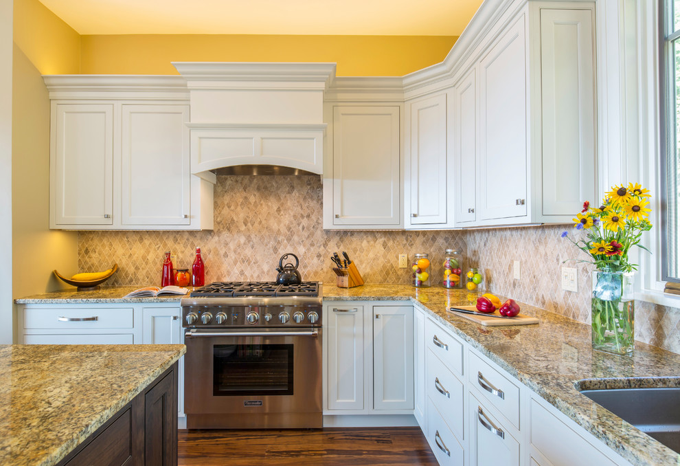 Inredning av ett klassiskt mellanstort kök, med en undermonterad diskho, släta luckor, gula skåp, granitbänkskiva, beige stänkskydd, stänkskydd i stenkakel, rostfria vitvaror, mellanmörkt trägolv och en köksö