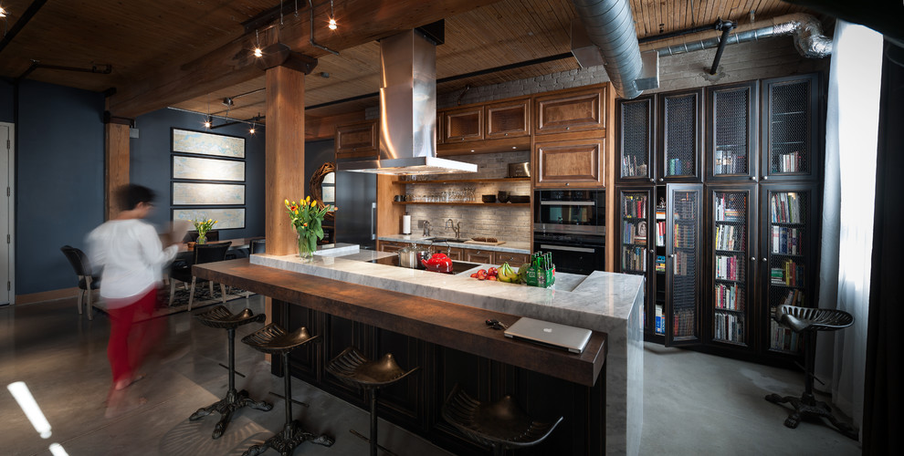 Industriell inredning av ett kök och matrum, med en undermonterad diskho, luckor med upphöjd panel, skåp i mellenmörkt trä, betonggolv, en köksö och rostfria vitvaror