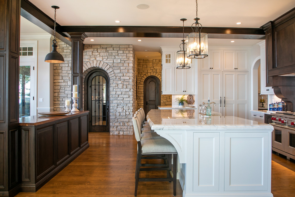 Large beach style kitchen in Milwaukee with white cabinets, quartz worktops, stainless steel appliances, multiple islands, white worktops, shaker cabinets and medium hardwood flooring.