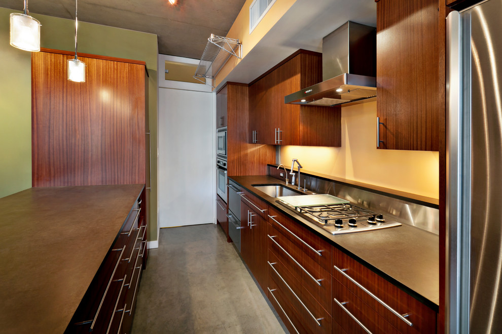 Foto di una cucina design con lavello sottopiano, ante lisce, ante in legno bruno, top in granito, paraspruzzi a effetto metallico e elettrodomestici in acciaio inossidabile