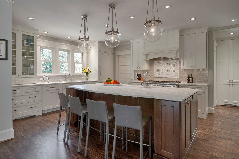 Design ideas for a large traditional l-shaped kitchen/diner in Seattle with shaker cabinets, white cabinets, grey splashback, metro tiled splashback, stainless steel appliances, dark hardwood flooring, an island, a submerged sink, marble worktops, brown floors and white worktops.