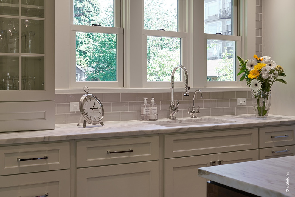 Bild på ett stort amerikanskt vit vitt kök, med en undermonterad diskho, skåp i shakerstil, vita skåp, rostfria vitvaror, mörkt trägolv, en köksö, beige stänkskydd, stänkskydd i keramik, marmorbänkskiva och brunt golv