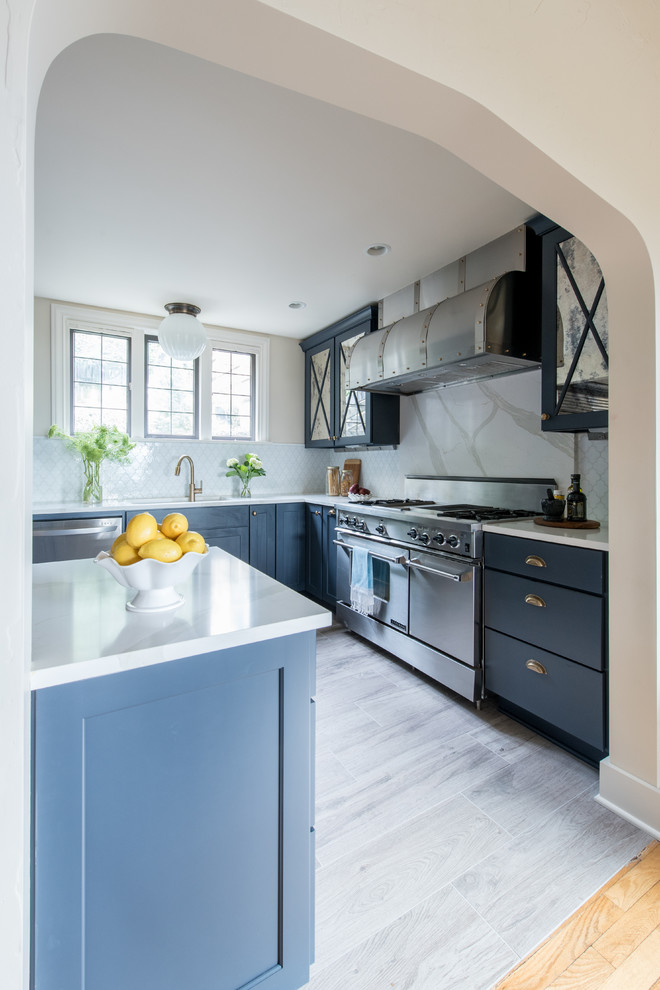 This is an example of a medium sized traditional galley enclosed kitchen in Seattle with a submerged sink, shaker cabinets, blue cabinets, engineered stone countertops, white splashback, glass tiled splashback, stainless steel appliances, porcelain flooring and an island.