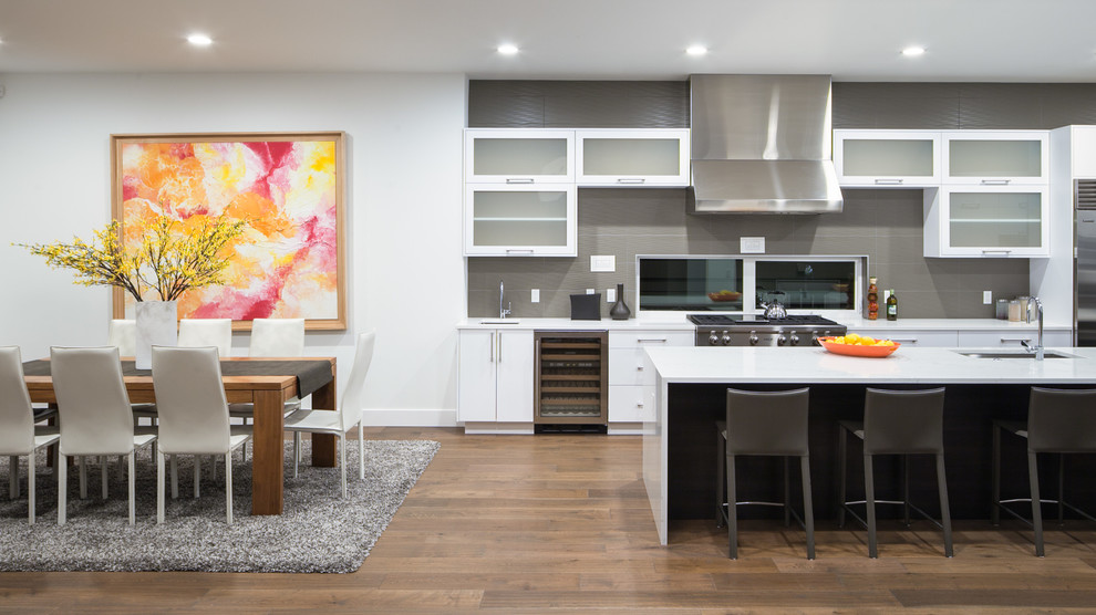 Offene, Zweizeilige Moderne Küche mit Unterbauwaschbecken, Glasfronten, weißen Schränken, Küchenrückwand in Grau, Küchengeräten aus Edelstahl, braunem Holzboden und Kücheninsel in Seattle