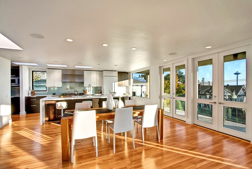 На фото: большая прямая кухня в стиле модернизм с обеденным столом, плоскими фасадами, белыми фасадами, зеленым фартуком, белой техникой, паркетным полом среднего тона и островом с