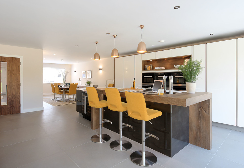 Große Moderne Wohnküche mit flächenbündigen Schrankfronten, weißen Schränken, Arbeitsplatte aus Holz, Keramikboden, Kücheninsel, grauem Boden und schwarzer Arbeitsplatte in Cambridgeshire