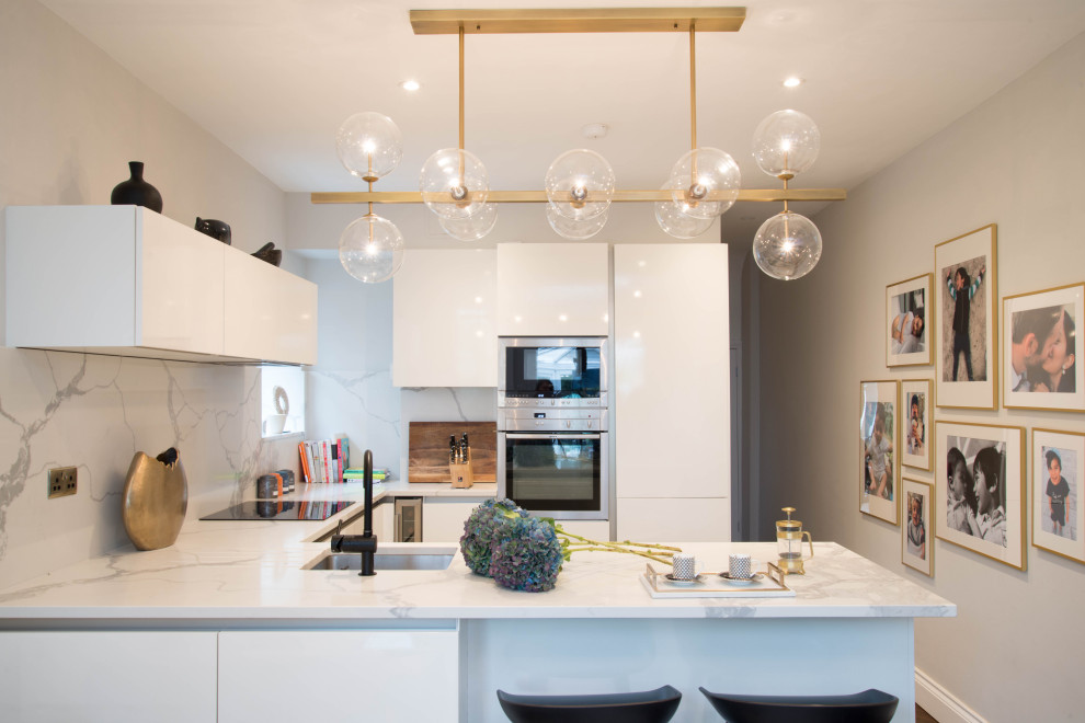 Photo of a medium sized contemporary u-shaped kitchen in London with a submerged sink, flat-panel cabinets, white cabinets, white splashback, a breakfast bar and white worktops.