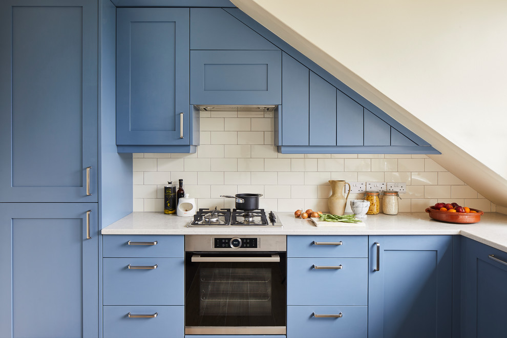 Bild på ett vintage vit vitt l-kök, med skåp i shakerstil, blå skåp, vitt stänkskydd, stänkskydd i tunnelbanekakel och rostfria vitvaror