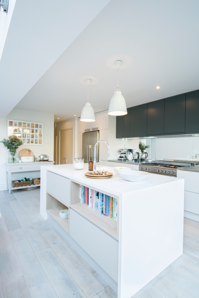 Mittelgroße, Zweizeilige Skandinavische Wohnküche mit flächenbündigen Schrankfronten, Küchengeräten aus Edelstahl, hellem Holzboden und Kücheninsel in London