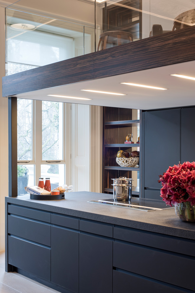 Expansive midcentury galley open plan kitchen in London with a built-in sink, glass-front cabinets, black cabinets, glass worktops, black splashback, porcelain splashback, integrated appliances, an island and black worktops.