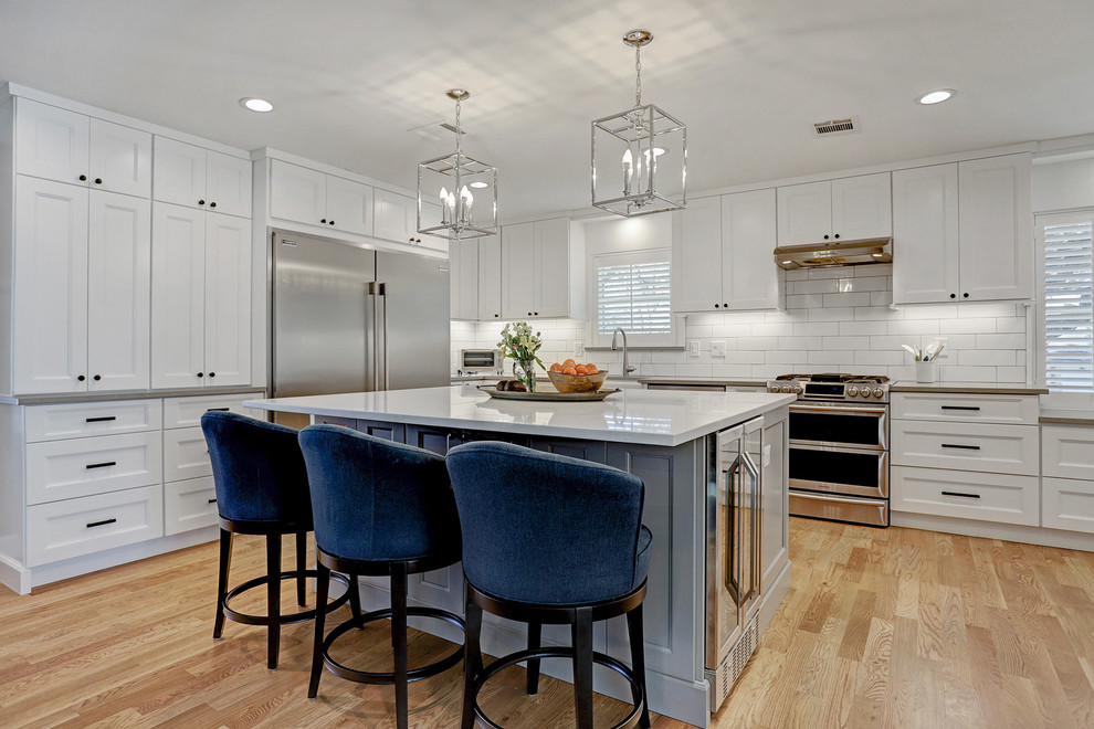 Medium sized classic l-shaped kitchen in Houston with recessed-panel cabinets, white cabinets, white splashback, stainless steel appliances, medium hardwood flooring, an island, brown floors and grey worktops.