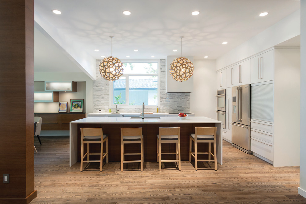 Inspiration for a mid-sized contemporary single-wall medium tone wood floor and brown floor open concept kitchen remodel in Other with an undermount sink, flat-panel cabinets, white cabinets, stainless steel appliances, an island, gray backsplash and matchstick tile backsplash