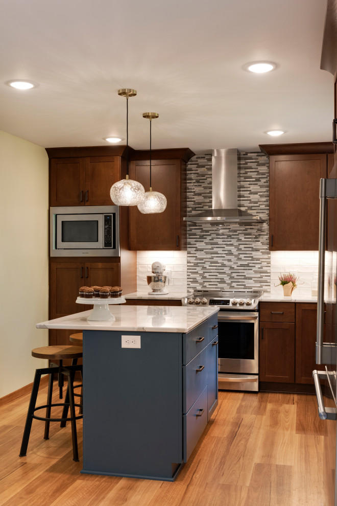Medium sized traditional l-shaped kitchen in Minneapolis with a submerged sink, shaker cabinets, engineered stone countertops, grey splashback, stainless steel appliances, medium hardwood flooring, an island, brown floors, white worktops, medium wood cabinets and matchstick tiled splashback.