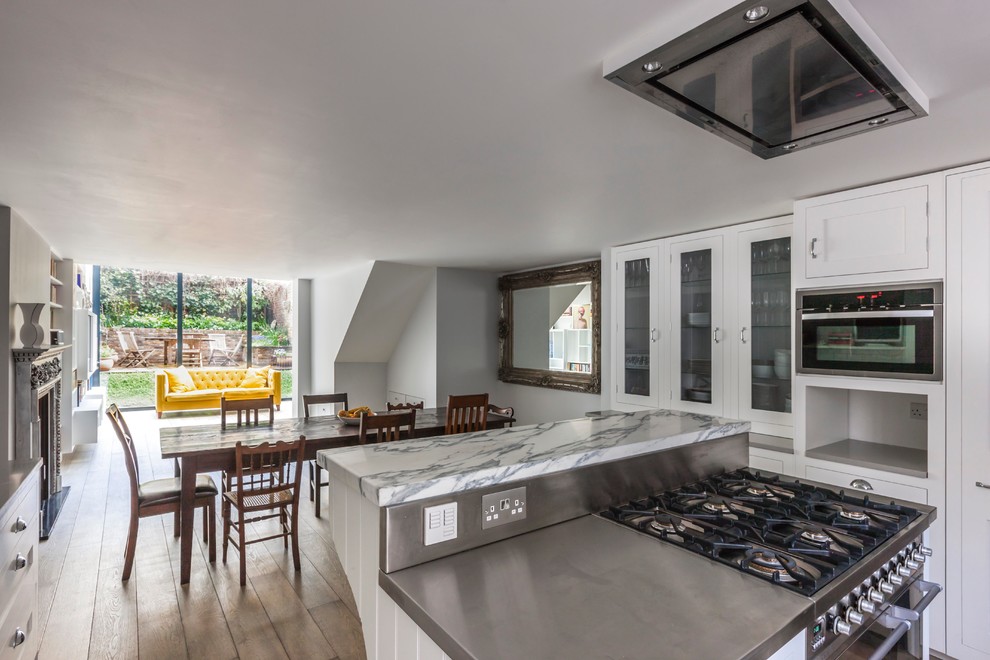This is an example of a large contemporary open plan kitchen in London with a submerged sink, marble worktops, white splashback, stainless steel appliances and medium hardwood flooring.