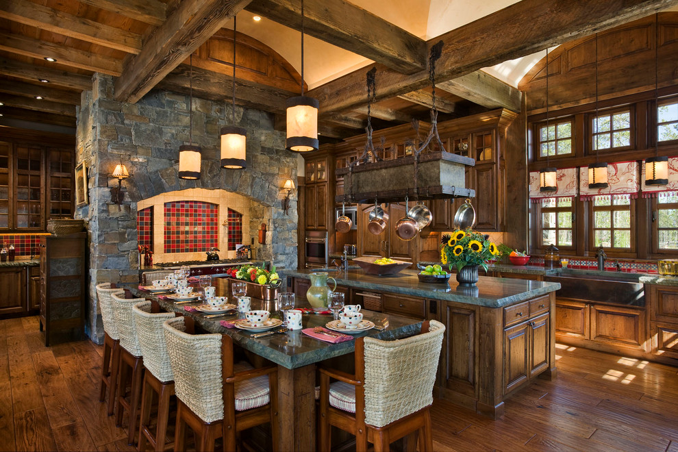 Aménagement d'une cuisine américaine montagne en bois foncé avec un placard avec porte à panneau surélevé et une crédence rouge.