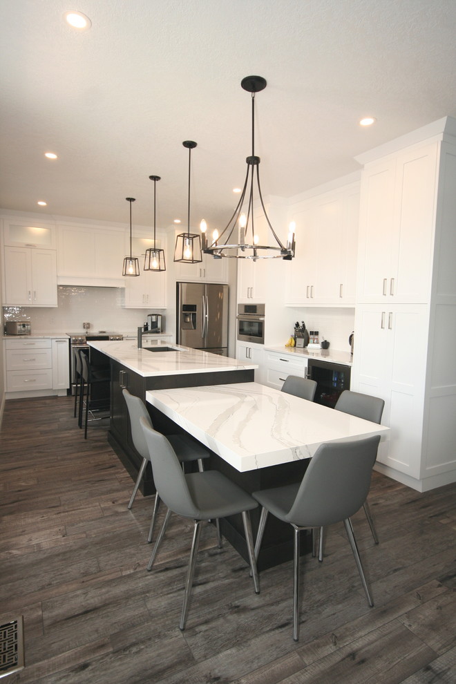 Example of a trendy l-shaped vinyl floor eat-in kitchen design with an undermount sink, shaker cabinets, white cabinets, granite countertops, white backsplash, subway tile backsplash, stainless steel appliances and white countertops