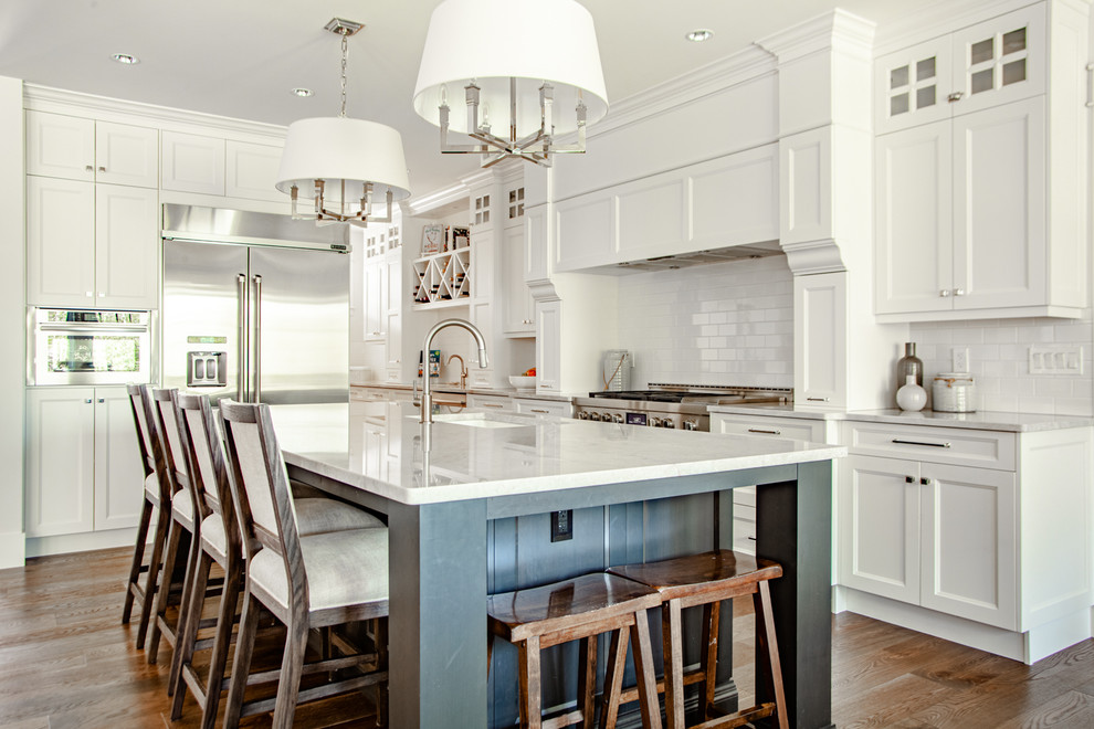 Inredning av ett amerikanskt mycket stort grå grått kök, med en undermonterad diskho, släta luckor, vita skåp, granitbänkskiva, vitt stänkskydd, stänkskydd i tunnelbanekakel, rostfria vitvaror, mellanmörkt trägolv, en köksö och brunt golv