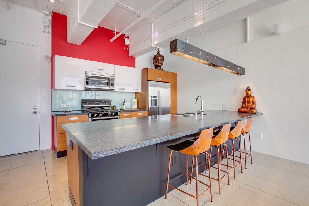 Example of an urban galley concrete floor open concept kitchen design in Los Angeles with a double-bowl sink, flat-panel cabinets, medium tone wood cabinets, blue backsplash, glass tile backsplash, stainless steel appliances and an island
