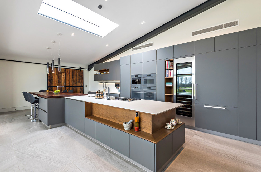 Cette photo montre une cuisine ouverte parallèle tendance avec un placard à porte plane, îlot, des portes de placard grises, un électroménager en acier inoxydable, un sol gris et un plan de travail blanc.